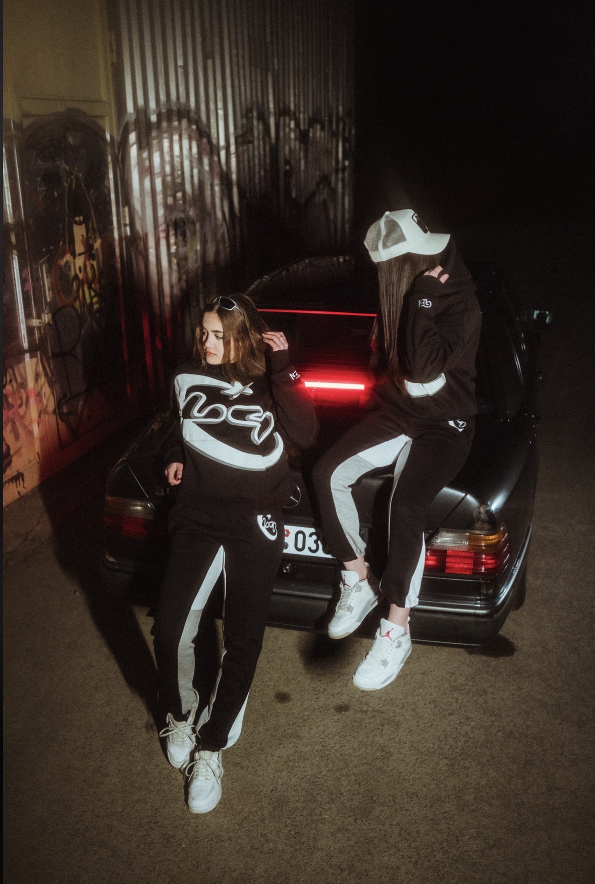 Two models by a car in a red-lit garage